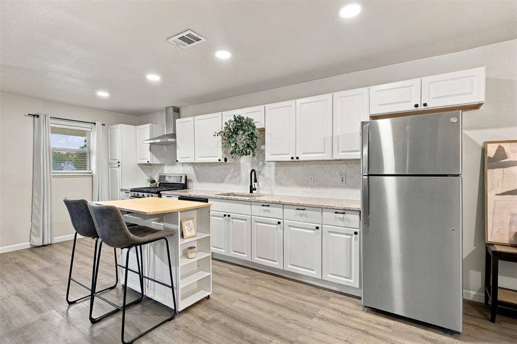 White cabinetry, wood-finish flooring, stainless steel appliances, recessed lighting, and a kitchen island with built-in shelving