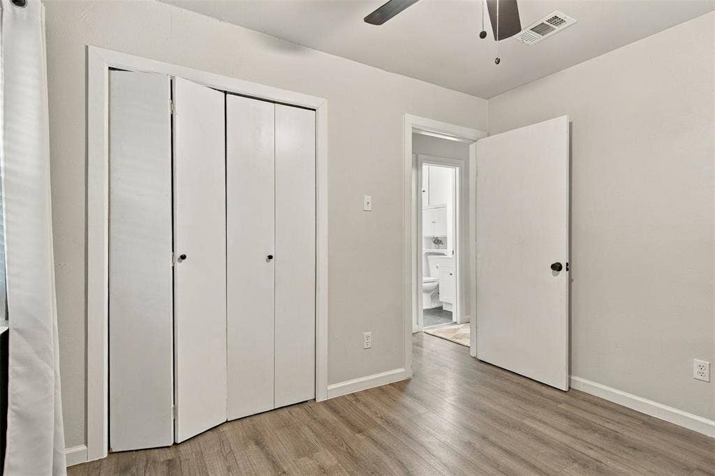 Wood-finish flooring, white bifold closet doors, light neutral wall paint, overhead ceiling fan, and white trim throughout