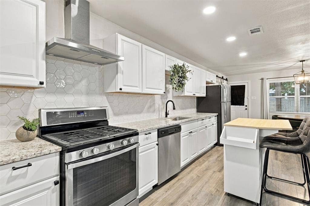 White shaker-style cabinetry, stainless steel appliances, light-toned wood-finish flooring, hexagonal tile backsplash, and recessed lighting