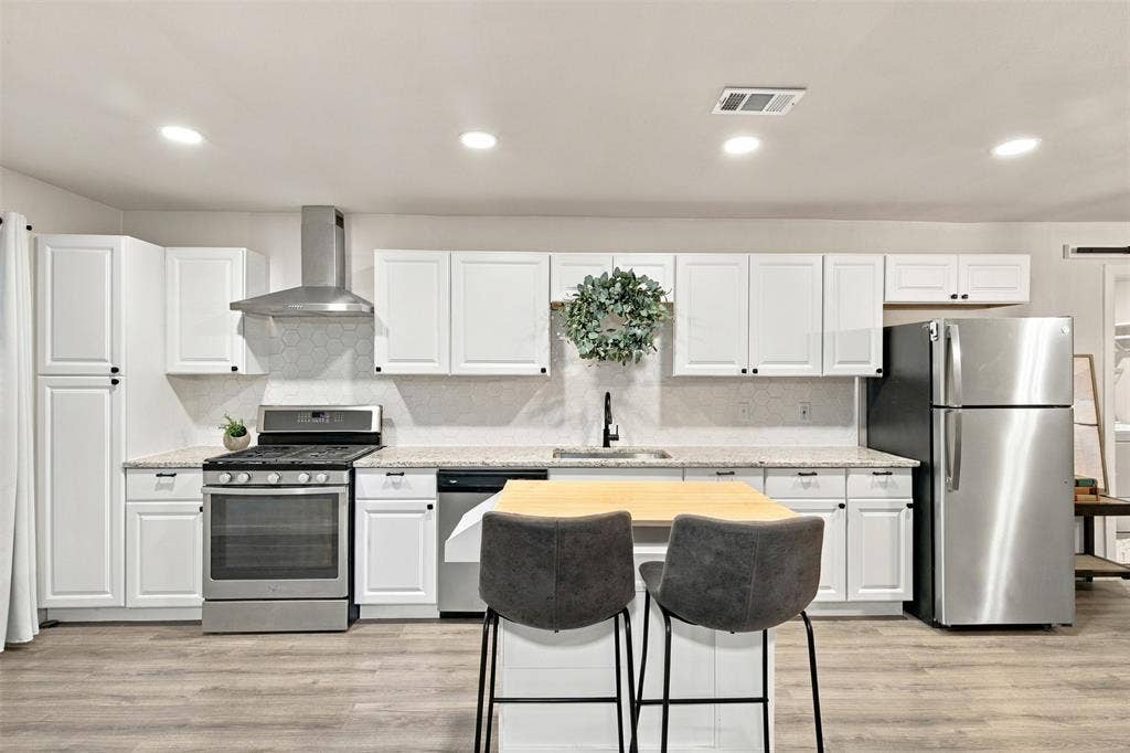 Kitchen featuring white cabinetry, stainless steel appliances, light-toned countertops, a geometric tile backsplash, and wood-finish flooring