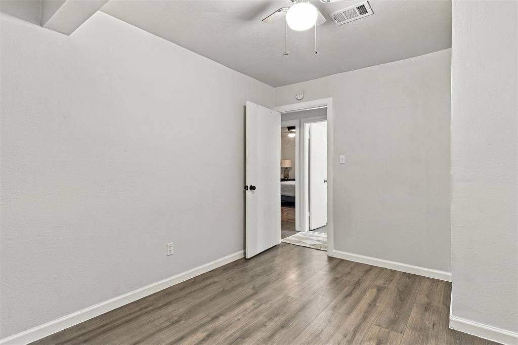 Wood-finish flooring with white trim, a ceiling fan with light fixture, and a white interior door with black hardware