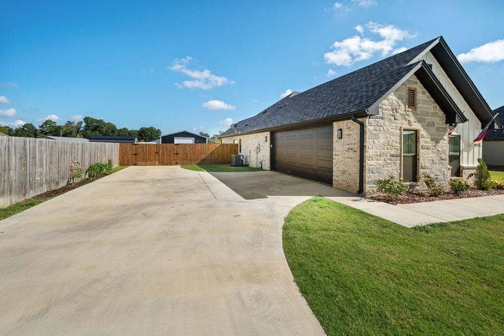 16139 Eagle Lane, Lindale, TX 75771 Stone exterior with dark trim accents, attached garage with a dark wood-finish door, concrete driveway, and manicured lawn