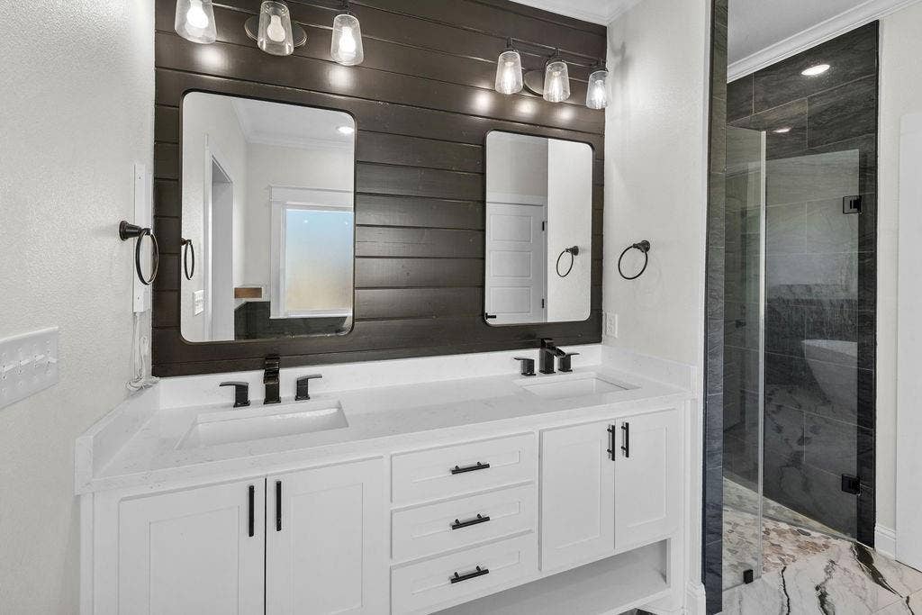 16139 Eagle Lane, Lindale, TX 75771 Dual vanity with white cabinetry and integrated sinks, matte black fixtures, dark wood-finish accent wall, and a separate glass-enclosed shower with tiled walls and floor