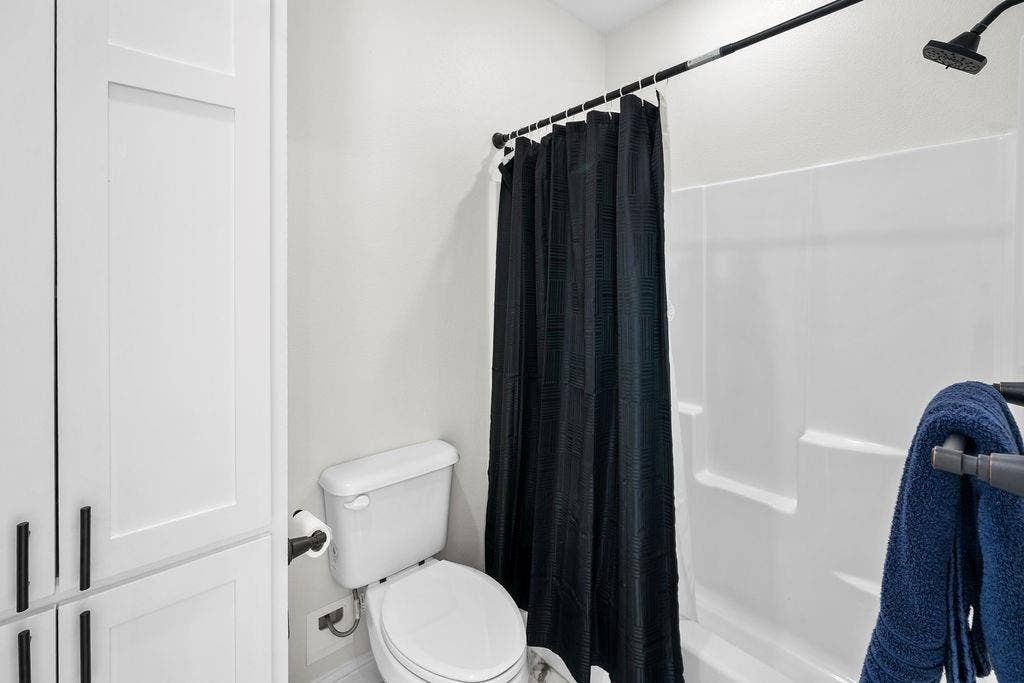16139 Eagle Lane, Lindale, TX 75771 White paneled cabinetry with dark hardware, a white toilet, and a shower with a white surround and dark-finish showerhead