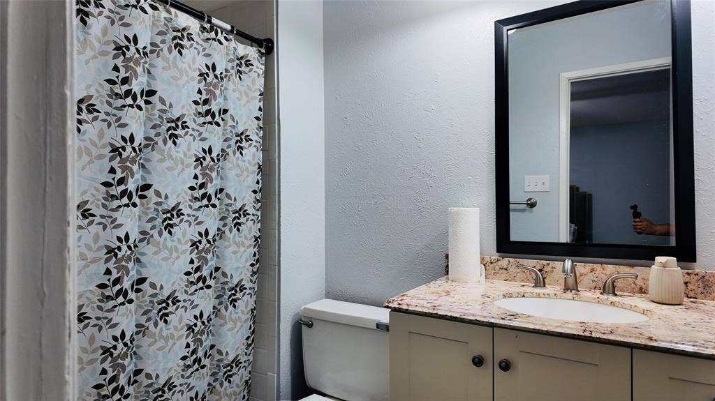 6541 Santa Fe Trail, Plano, TX 75023 Vanity with a polished stone countertop and integrated sink, framed mirror, and a two-door cabinet with hardware