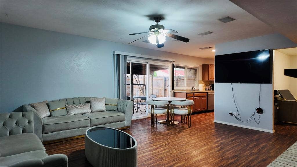 6541 Santa Fe Trail, Plano, TX 75023 Wood-finish flooring throughout, ceiling fan with integrated lighting, sliding glass door to exterior, kitchen area with wood cabinetry and stainless steel appliances, and built-in wall partition