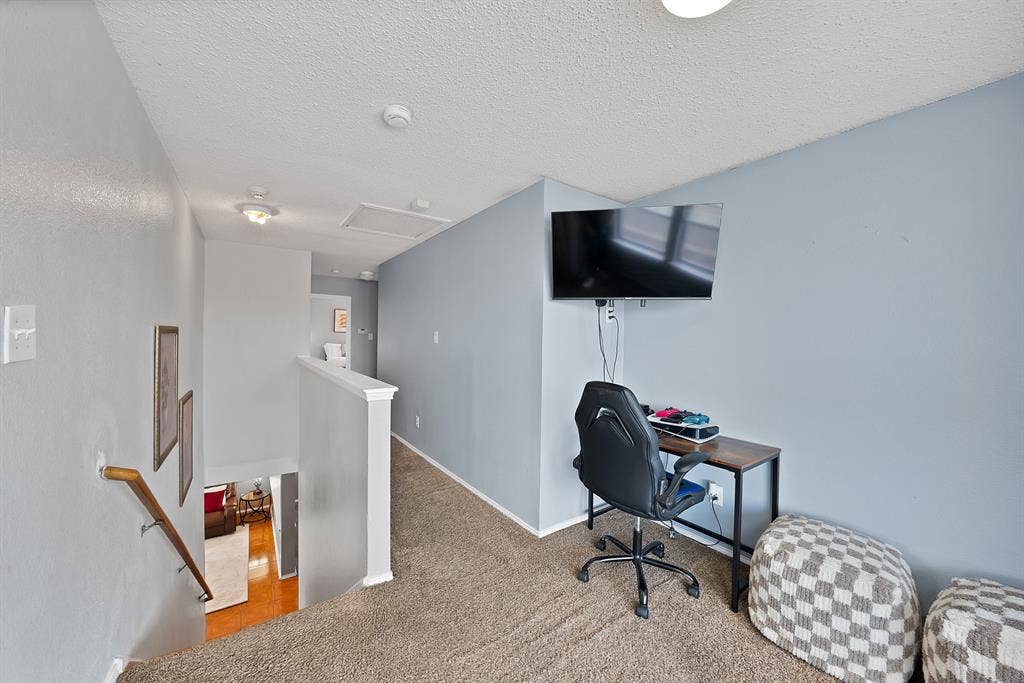 2326 Mcintosh Court, Lancaster, TX 75134 Carpeted upper-level landing with painted walls, a built-in wall-mounted television, a white banister, and an overhead light fixture