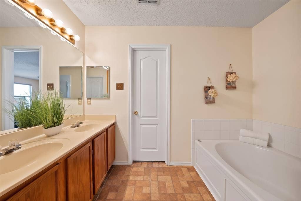 2326 Mcintosh Court, Lancaster, TX 75134 Double vanity with integrated sinks, wood-finish cabinetry, built-in bathtub with tiled surround, and a panel-style door