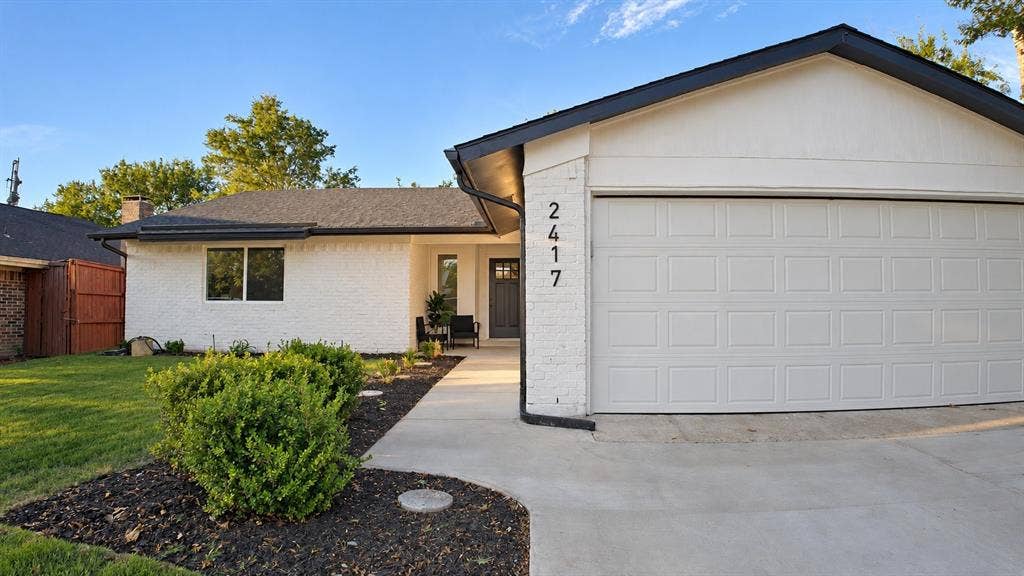 2417 Via Barcelona, Carrollton, TX 75006 White brick exterior with black trim, a paneled garage door, a concrete driveway, and a front walkway