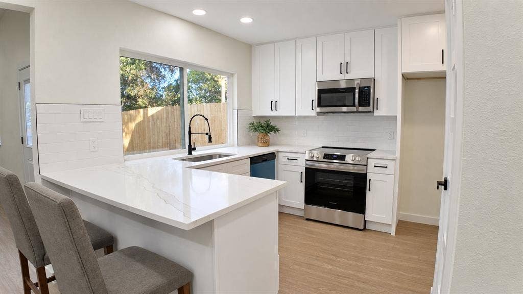 2417 Via Barcelona, Carrollton, TX 75006 White cabinetry with matte black hardware, stainless steel appliances, white subway tile backsplash, and light wood-finish flooring