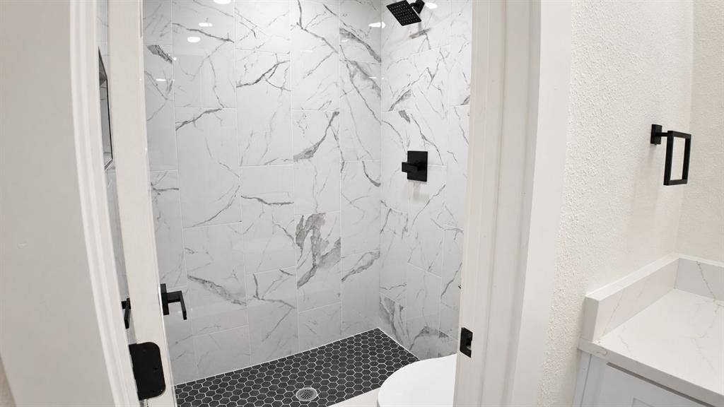 2417 Via Barcelona, Carrollton, TX 75006 Walk-in shower with black hexagonal tile flooring and white marble-look wall tiles