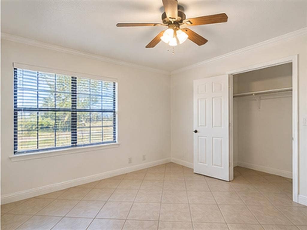 1919 American Drive, #B112, Lago Vista, TX 78645 Ceiling fan with light kit, crown molding, tile flooring, window with blinds, and a built-in closet with shelving