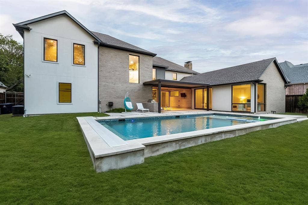 5724 Charlestown Drive, Dallas, TX 75230 Expansive swimming pool with a surrounding concrete and stone border, large grass area, covered patio, and extensive glass doors