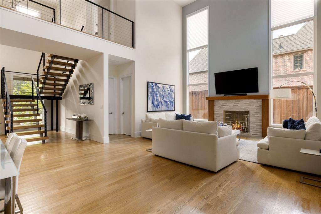 5724 Charlestown Drive, Dallas, TX 75230 Open-concept living area featuring high ceilings, wood-finish flooring, a contemporary floating staircase with cable railing, a stone-clad fireplace, and tall windows
