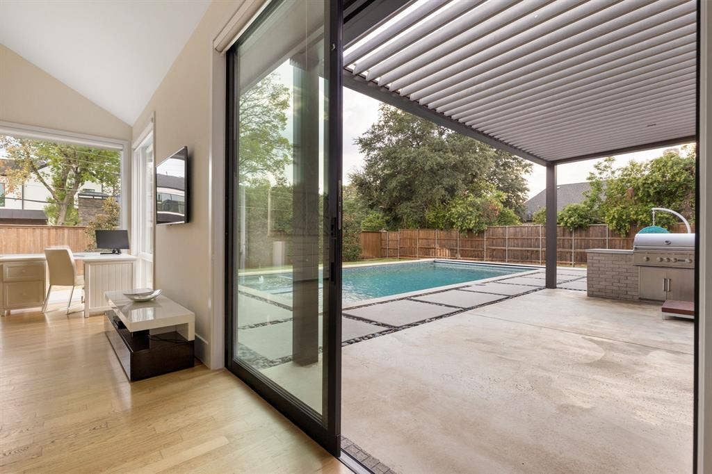 5724 Charlestown Drive, Dallas, TX 75230 Sliding glass door opening to a concrete patio with a built-in outdoor kitchen, an in-ground swimming pool, and a louvered patio cover