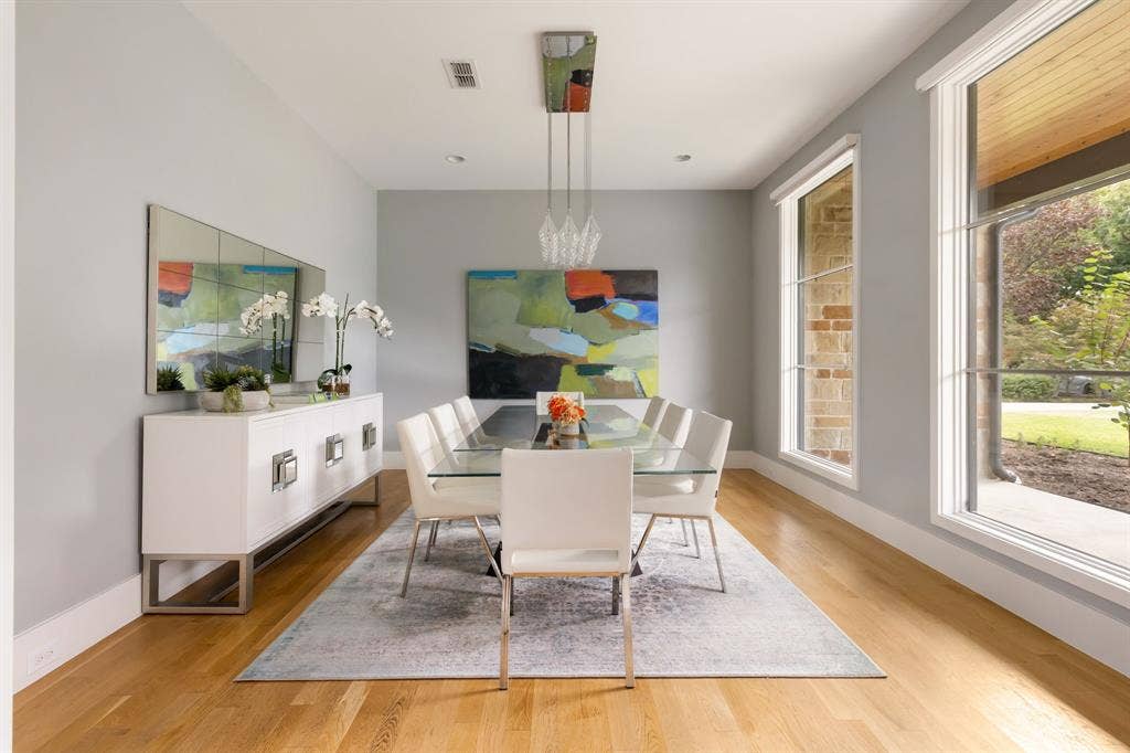 5724 Charlestown Drive, Dallas, TX 75230 Bright dining area showcasing hardwood flooring, a white pendant light fixture, and expansive windows framing natural landscaping