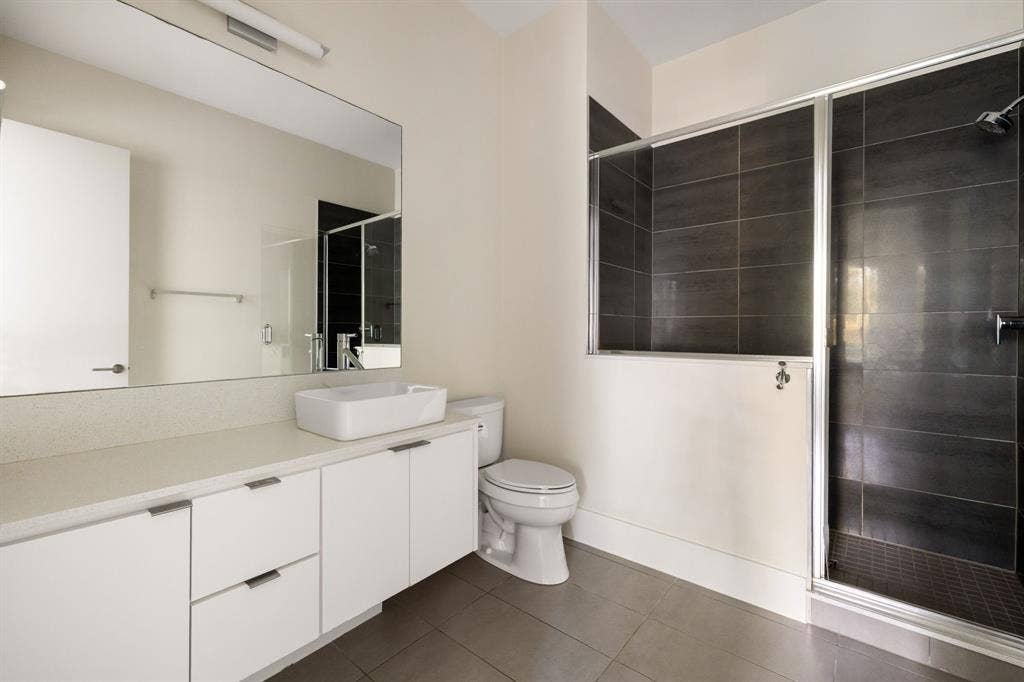 5724 Charlestown Drive, Dallas, TX 75230 Rectangular vessel sink, white cabinetry with silver-tone hardware, large vanity mirror, tile flooring, and a glass-enclosed shower with dark-tiled walls