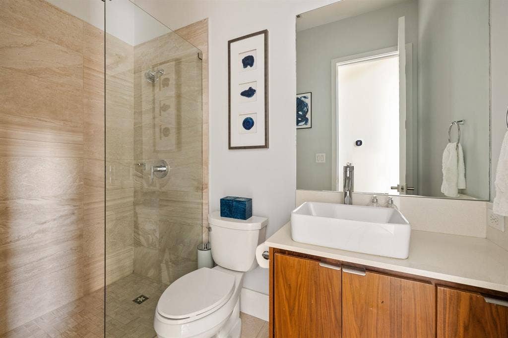 5724 Charlestown Drive, Dallas, TX 75230 Glass-enclosed shower with natural-toned tile surround, chrome fixtures, wood-finish vanity, white vessel sink, and an integrated countertop