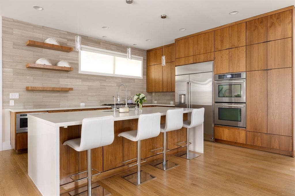 5724 Charlestown Drive, Dallas, TX 75230 Gourmet kitchen with wood-finish flooring, full-height wood cabinetry, stainless steel double ovens, stainless steel refrigerator, and an expansive island with a waterfall countertop