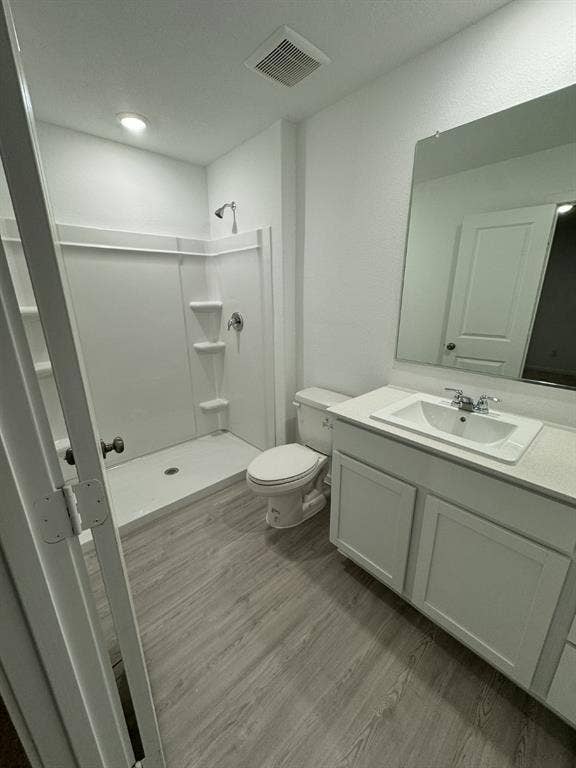7908 Gilbert Street, McKinney, TX 75071 Bathroom featuring light wood-finish flooring, a white vanity with panel-front cabinetry, a white rectangular sink, and a shower with built-in shelving