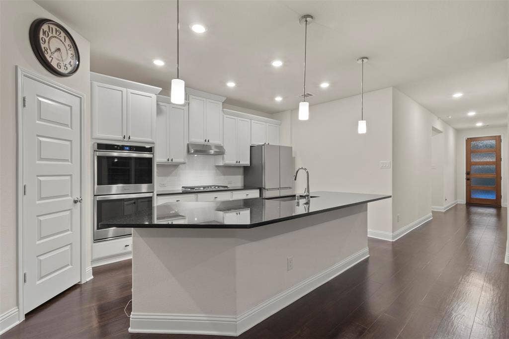 8028 Hickory Branch Drive, Frisco, TX 75034 Open-concept kitchen with a large island, white shaker cabinetry, stainless steel appliances, and dark wood-finish flooring