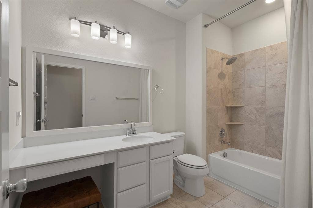 8028 Hickory Branch Drive, Frisco, TX 75034 White vanity with integrated sink, expansive framed mirror, contemporary four-light fixture, tub with tiled surround, and built-in shower shelving
