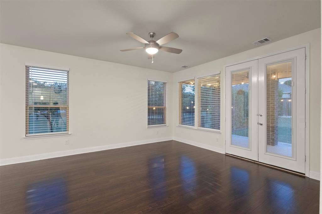 8028 Hickory Branch Drive, Frisco, TX 75034 Dark wood-finish flooring, white walls, multiple windows with blinds, double glass-paneled doors, and a ceiling fan with integrated lighting