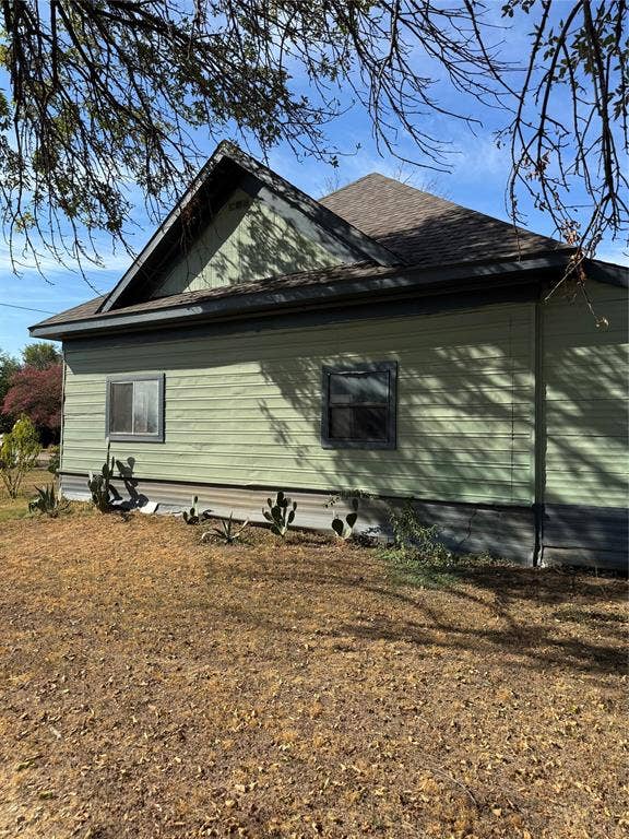 102 N 6th Street W, Dawson, TX 76639 Pitched shingle roof over a vinyl-sided exterior, featuring a stone foundation and established drought-tolerant plantings