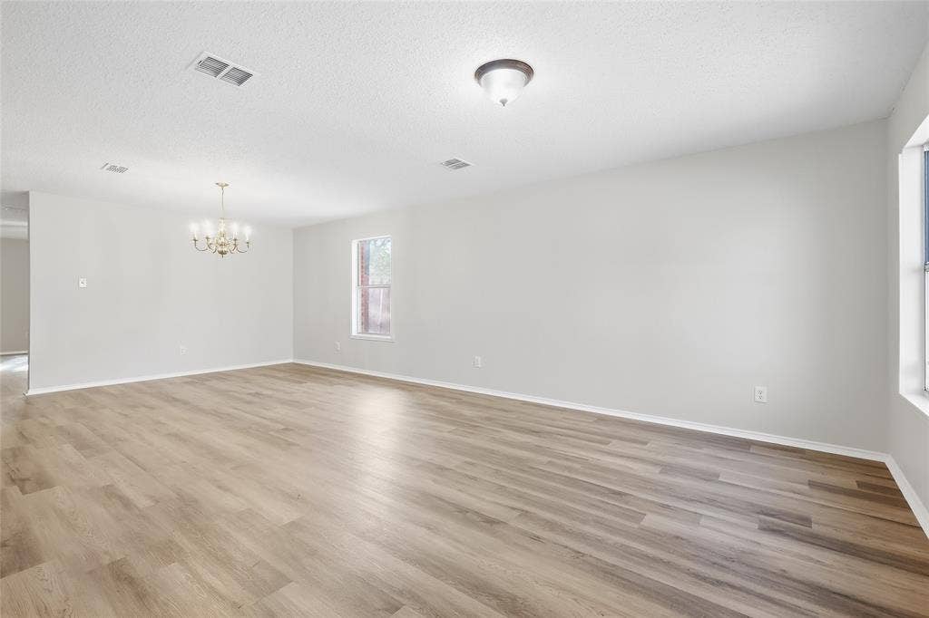 Spacious room with wood-finish flooring, two windows, a ceiling-mounted light fixture, and a decorative chandelier