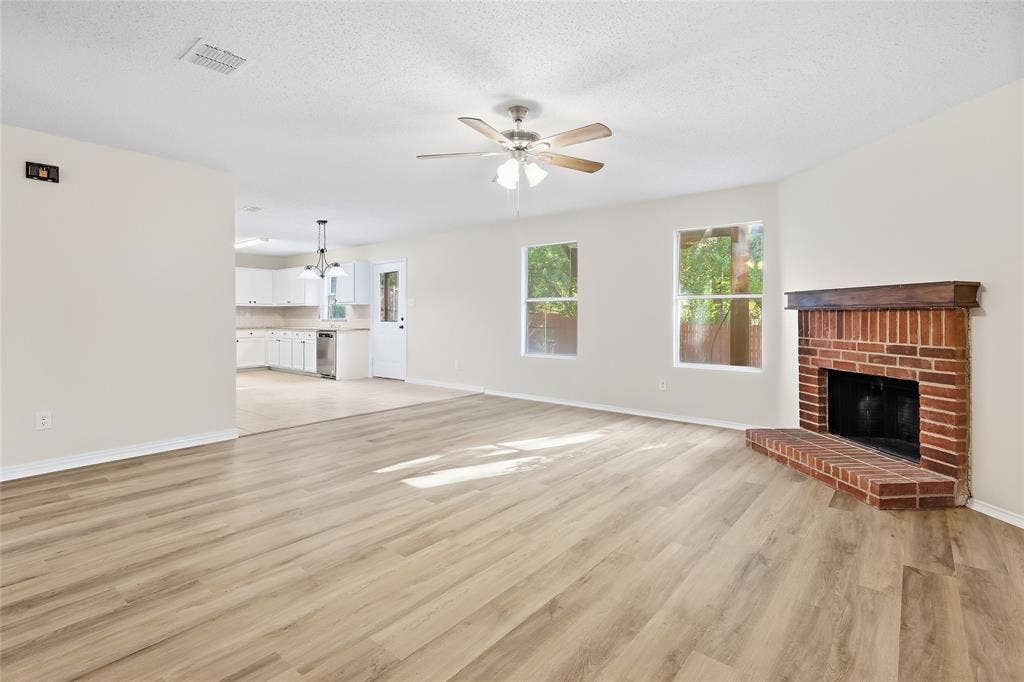 Spacious living area featuring wood-finish flooring, a brick fireplace with a wood mantle, and a ceiling fan