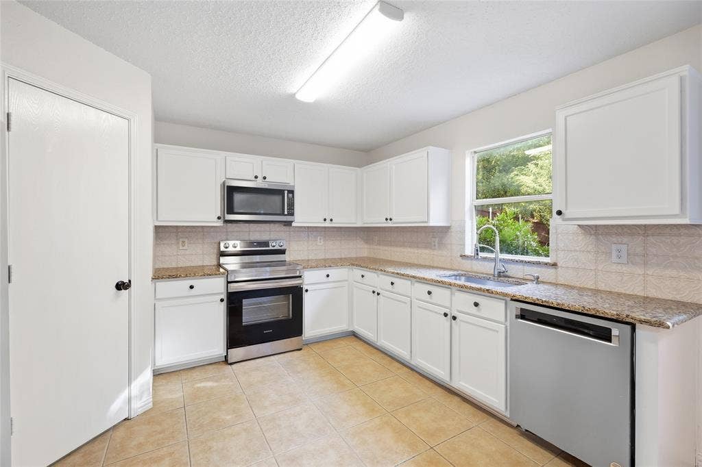 Kitchen featuring white cabinetry, granite countertops, stainless steel appliances, tile flooring, and a tile backsplash