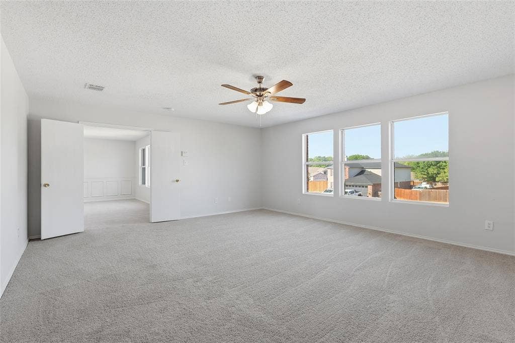 Expansive room with neutral carpet, three large windows, and a ceiling fan