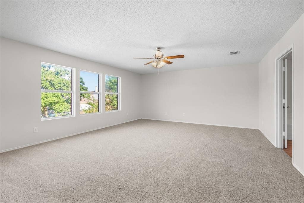 Spacious room featuring light-colored carpet, three windows, a ceiling fan with light, and white walls