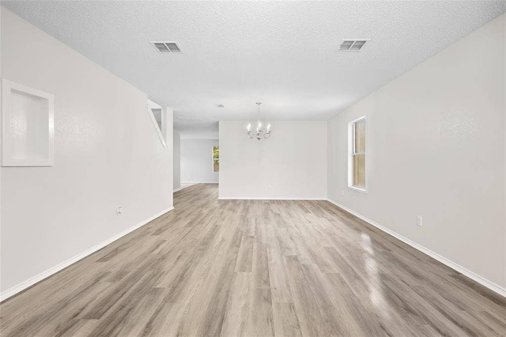 Wood-finish flooring throughout, white painted walls, and a multi-arm chandelier