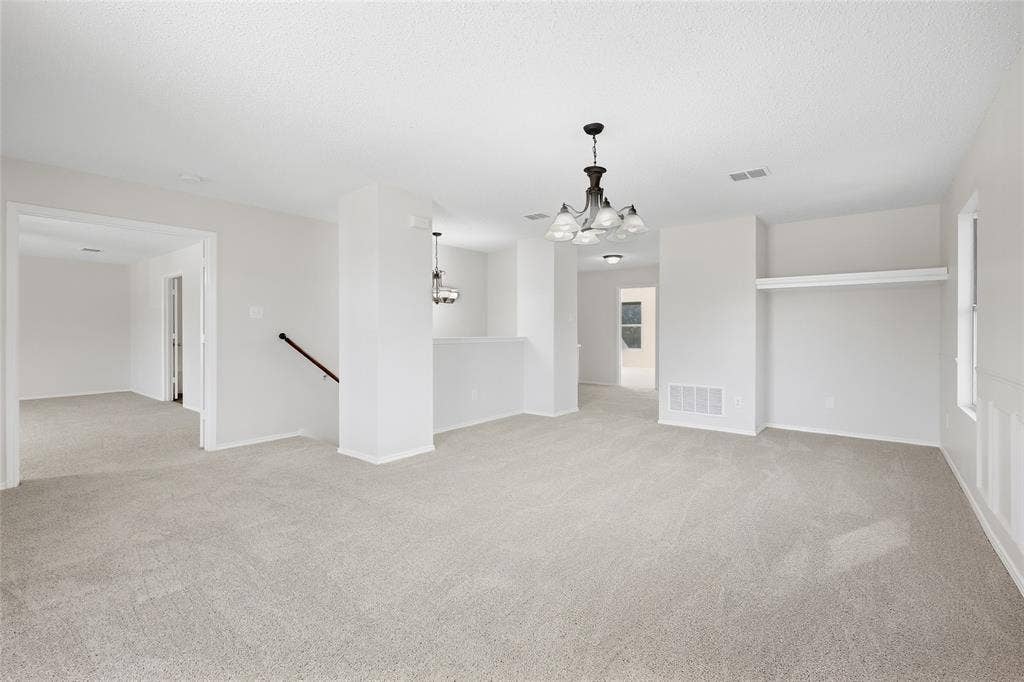 Expansive carpeted area with a decorative chandelier and white walls