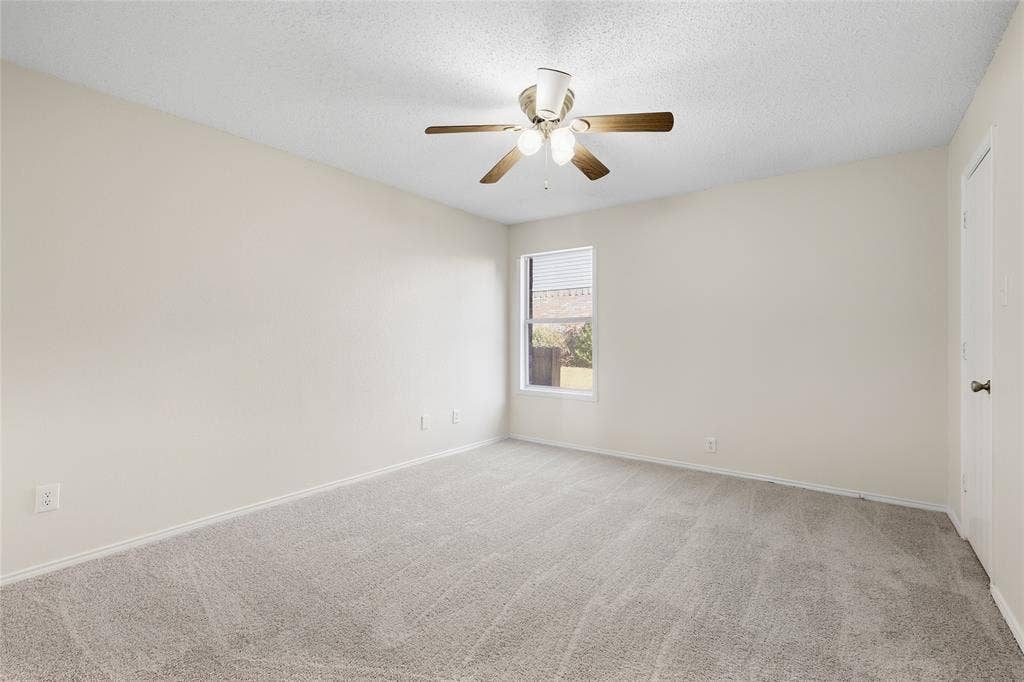 Wall-to-wall carpeting, window with blinds, ceiling fan with light fixture, and a solid door
