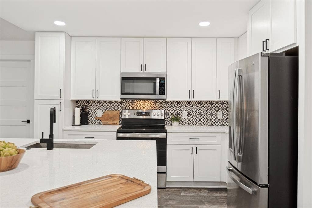 9038 Flicker Lane, Dallas, TX 75238 White shaker cabinetry, patterned tile backsplash, stainless steel appliances, white countertops, and wood-finish flooring