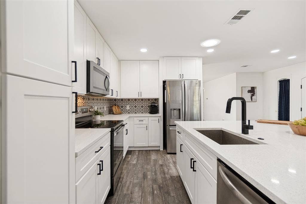9038 Flicker Lane, Dallas, TX 75238 Modern kitchen featuring white shaker cabinetry, stainless steel appliances, wood-finish flooring, and a large center island with an undermount sink and matte black faucet