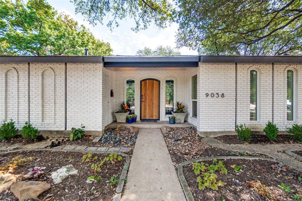 9038 Flicker Lane, Dallas, TX 75238 White brick exterior with a flat roofline, featuring an arched wooden entry door