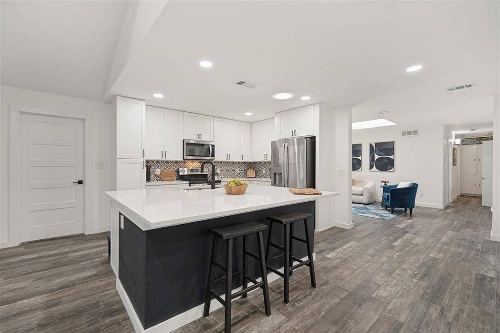 9038 Flicker Lane, Dallas, TX 75238 Kitchen featuring a central island with countertop seating, white cabinetry, integrated stainless steel appliances, and wood-finish flooring