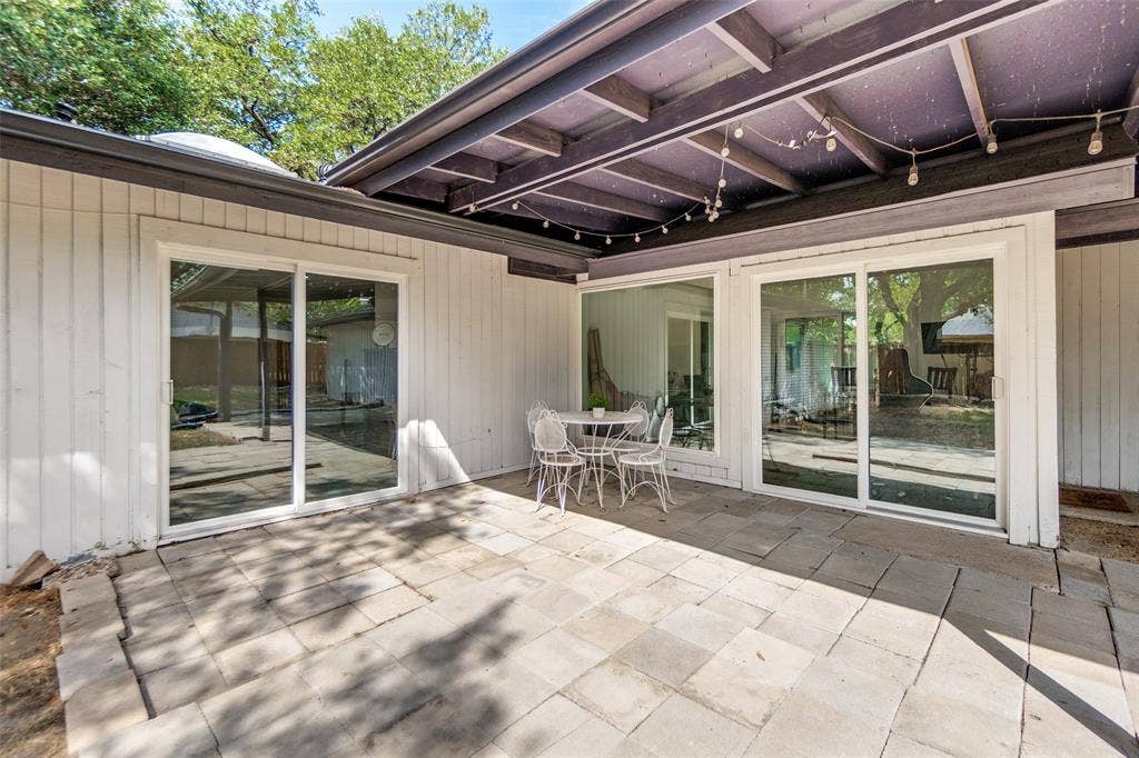 9038 Flicker Lane, Dallas, TX 75238 Paved patio with multiple sliding glass doors, a wood-beam overhang, and plank siding