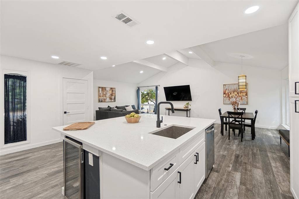 9038 Flicker Lane, Dallas, TX 75238 Open-concept living space with vaulted ceilings, wood-finish flooring, a kitchen island featuring a built-in beverage cooler, and recessed lighting