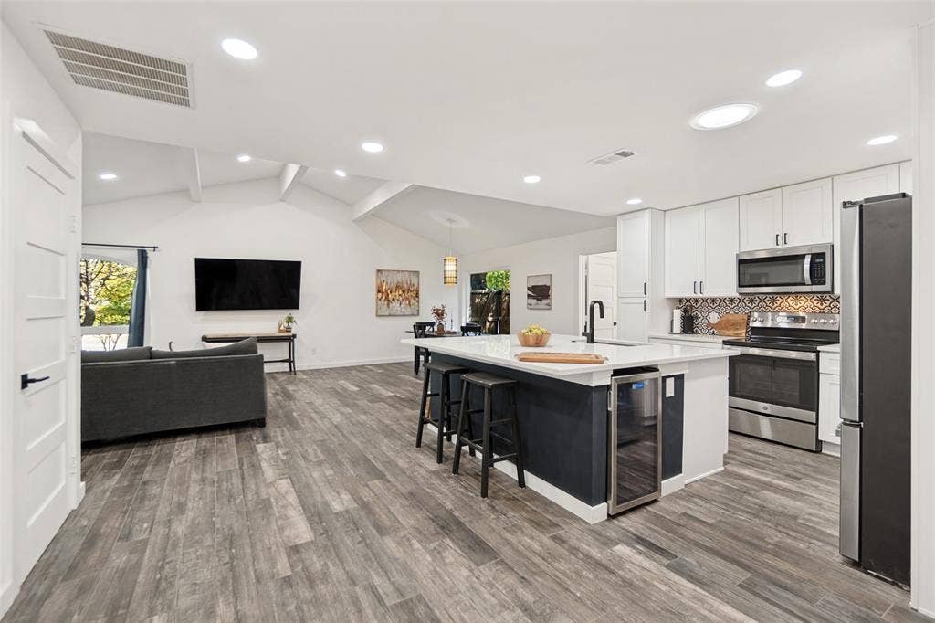 9038 Flicker Lane, Dallas, TX 75238 Vaulted ceilings, wood-finish flooring, white cabinetry, stainless steel appliances, and a kitchen island with built-in beverage refrigerator