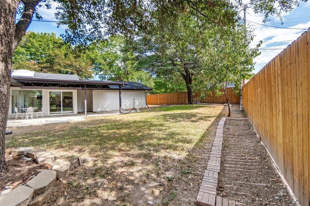 9038 Flicker Lane, Dallas, TX 75238 Expansive backyard featuring a privacy fence, covered patio, and large sliding glass doors