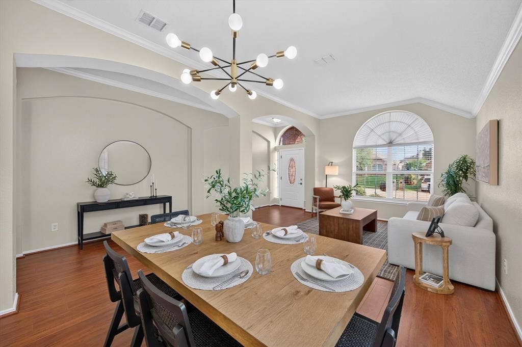 Dining area featuring wood-finish flooring, vaulted ceilings, arched architectural alcoves, a modern multi-arm chandelier, and a large arched window with integrated grilles