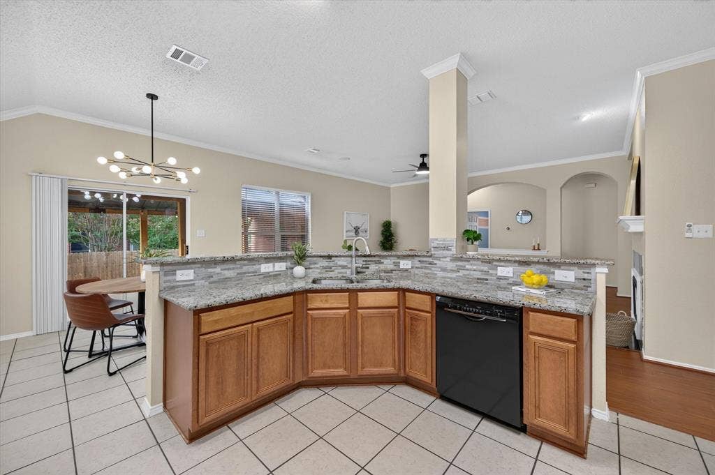 Kitchen featuring stone countertops, stone-tiled backsplash, built-in black dishwasher, wood cabinetry, and tile flooring