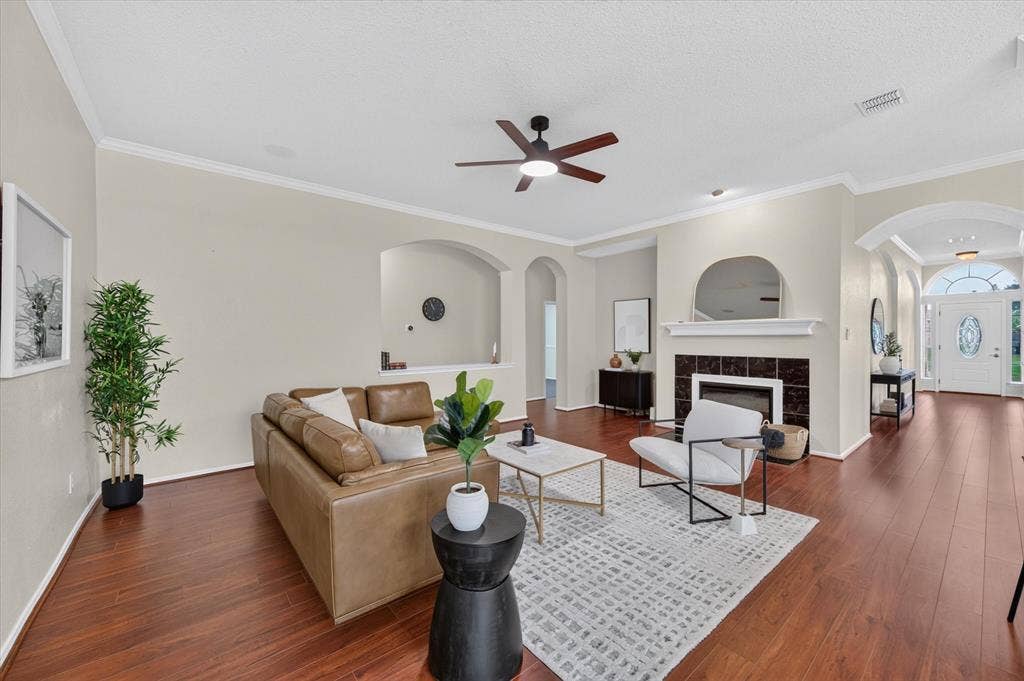 Living area featuring wood-finish flooring, a fireplace with a tile surround and mantel, arched wall niches, and a ceiling fan