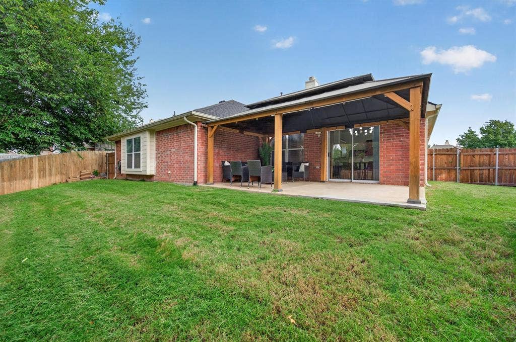 Rear exterior featuring red brick masonry, a covered patio with a wooden pergola, sliding glass doors, and wooden privacy fencing