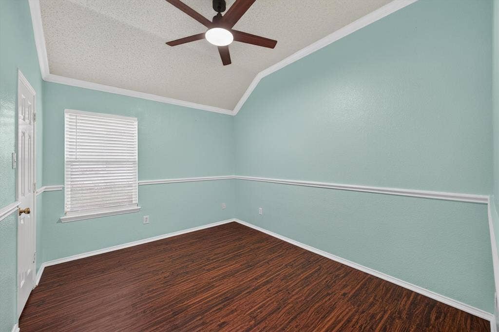 Room featuring vaulted ceilings, wood-finish flooring, a central ceiling fan with integrated lighting, a window with horizontal blinds, and chair rail molding