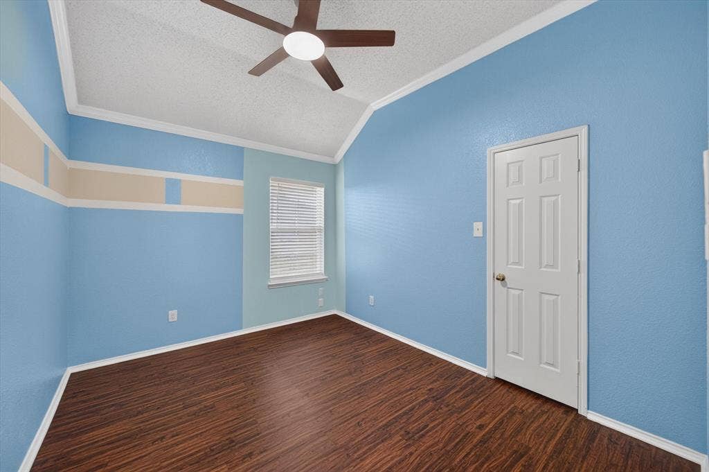 Vaulted ceiling room featuring wood-finish flooring, a ceiling fan with integrated lighting, and a six-panel door